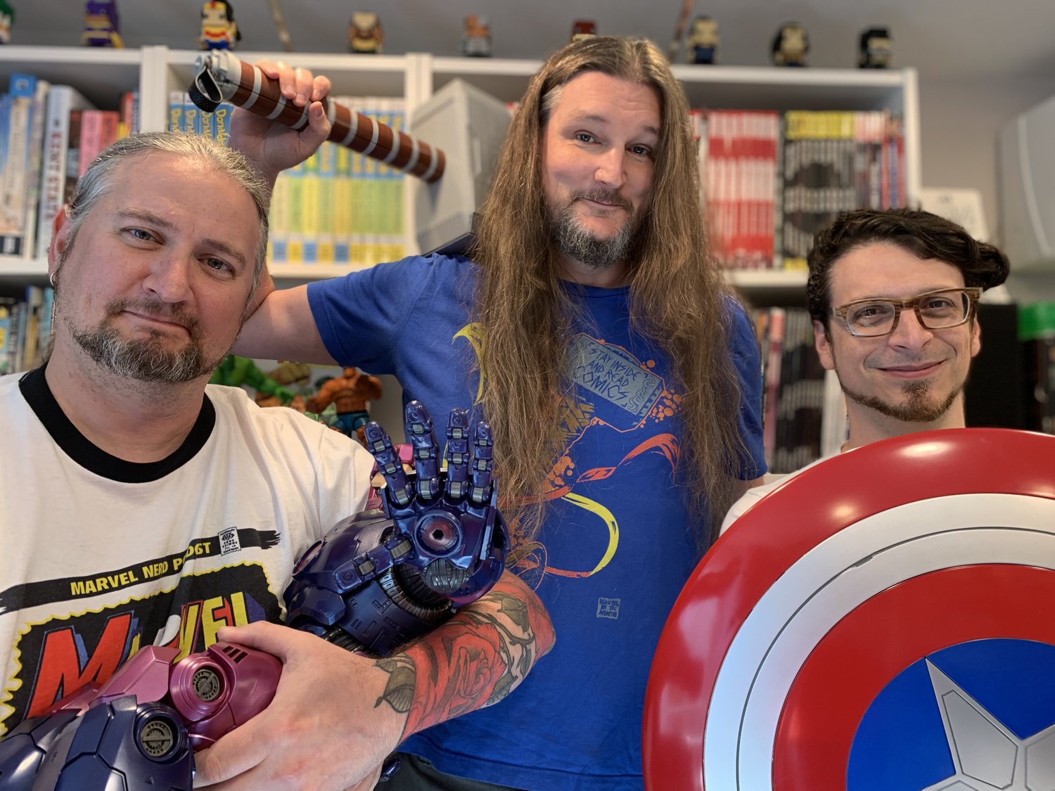 Bryan, Robb, and Jamie posing with a Sentinel, Mjolnir, and Captain America's shield in front of a wall of comic books on shelves.